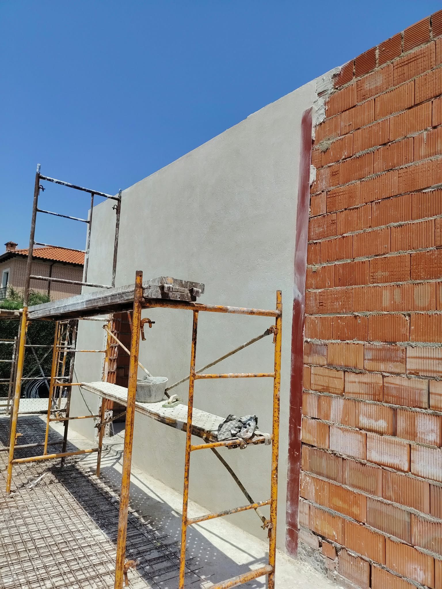 Andamios junto a un muro de ladrillos en construcción, con el exterior parcialmente enlucido y cielo azul.
