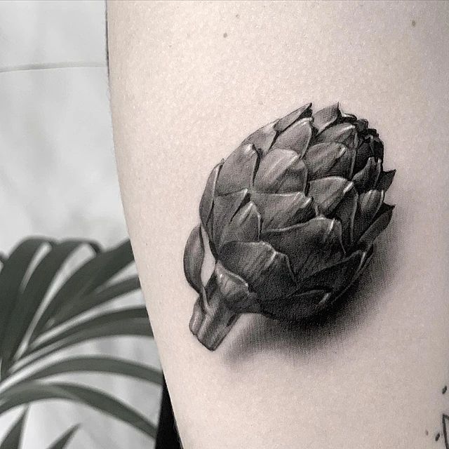 Un tatuaje en blanco y negro de una alcachofa en la pierna de una persona.