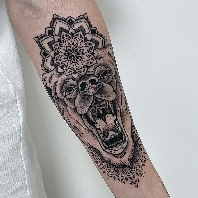 Un tatuaje en blanco y negro de un oso con un mandala en la cabeza.
