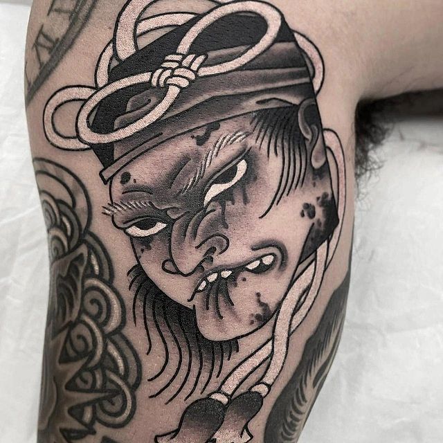 Un tatuaje en blanco y negro de la cara de un hombre con un pañuelo en la cabeza.