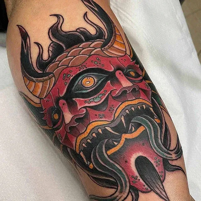 Un tatuaje de un demonio con cuernos y barba en el brazo de una persona.