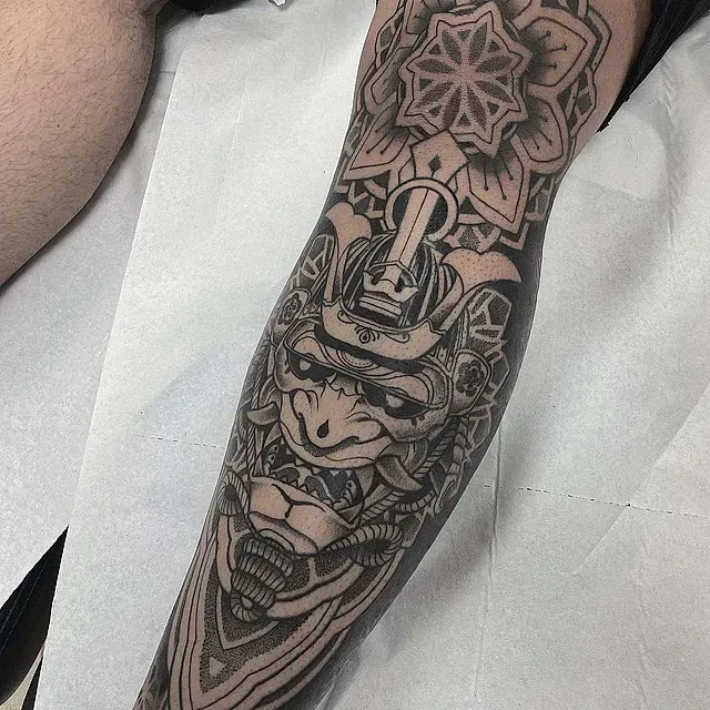 Un hombre tiene un tatuaje de un samurái en su antebrazo.