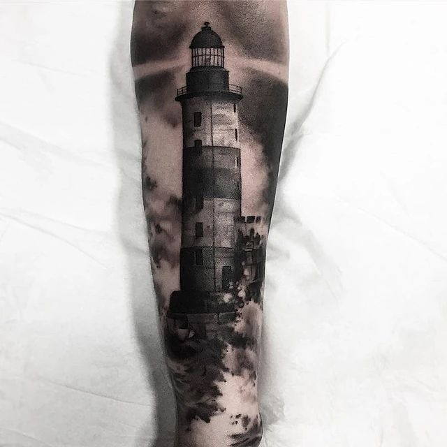 Un tatuaje en blanco y negro de un faro en la pierna de una persona.