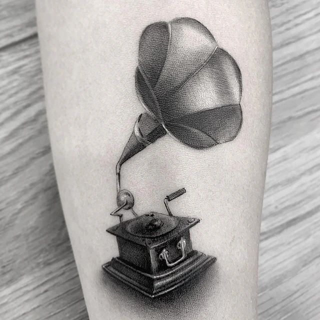 Un tatuaje en blanco y negro de un antiguo fonógrafo en la pierna de una persona.