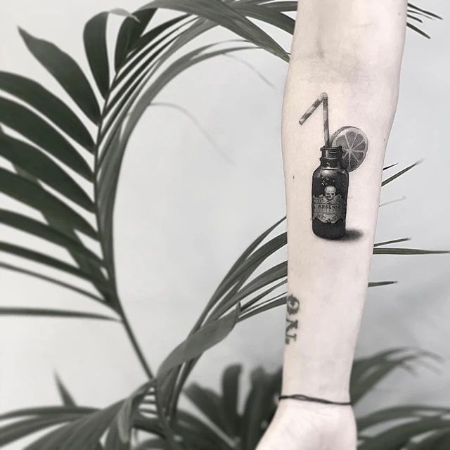 Una persona tiene un tatuaje de una botella con una pajita en el antebrazo.