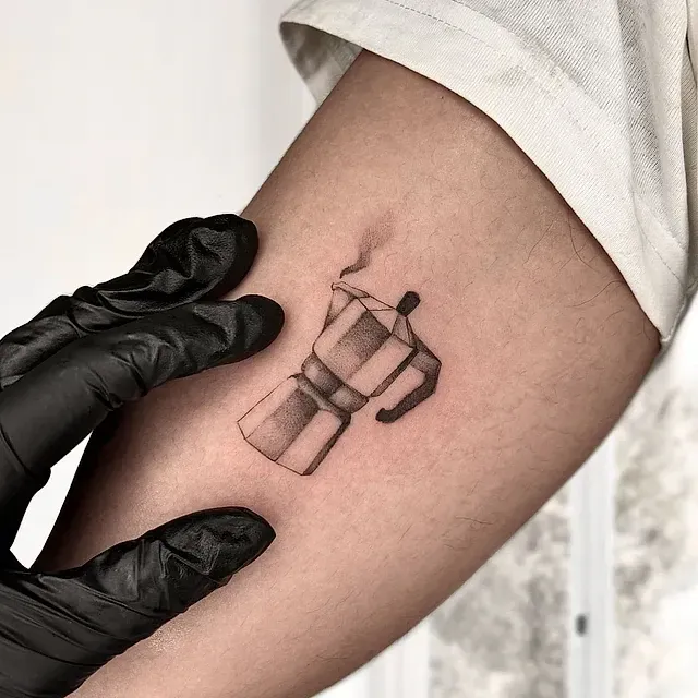 Una persona tiene un pequeño tatuaje de una cafetera en el brazo.