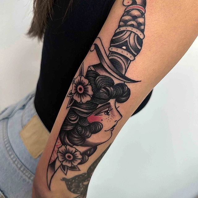 Una mujer tiene un tatuaje de la cara de una mujer y una daga en el brazo.