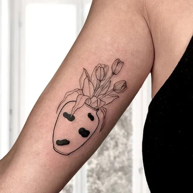 Una mujer tiene un tatuaje de flores en un jarrón en su brazo.