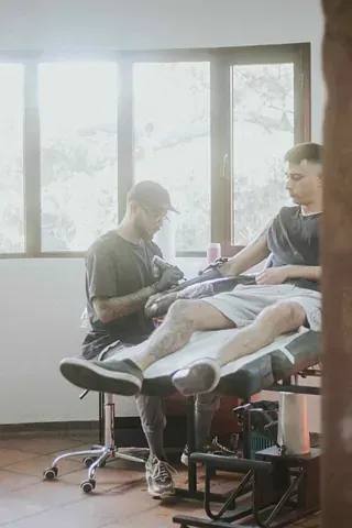Un hombre se hace un tatuaje en la pierna de otro hombre.
