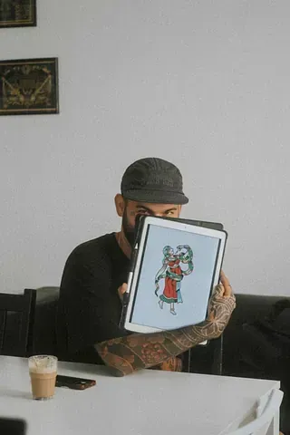 Un hombre está sentado en una mesa sosteniendo una tableta con una imagen de un gato en ella.