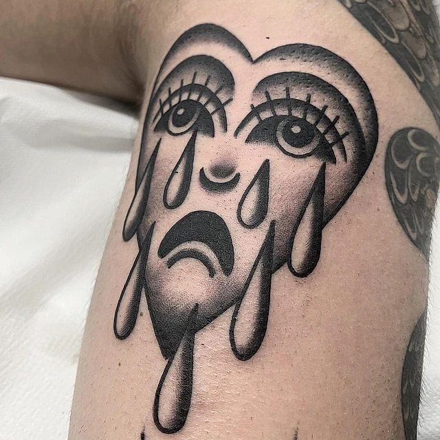 Un tatuaje en blanco y negro de una cara llorando con lágrimas saliendo de sus ojos.