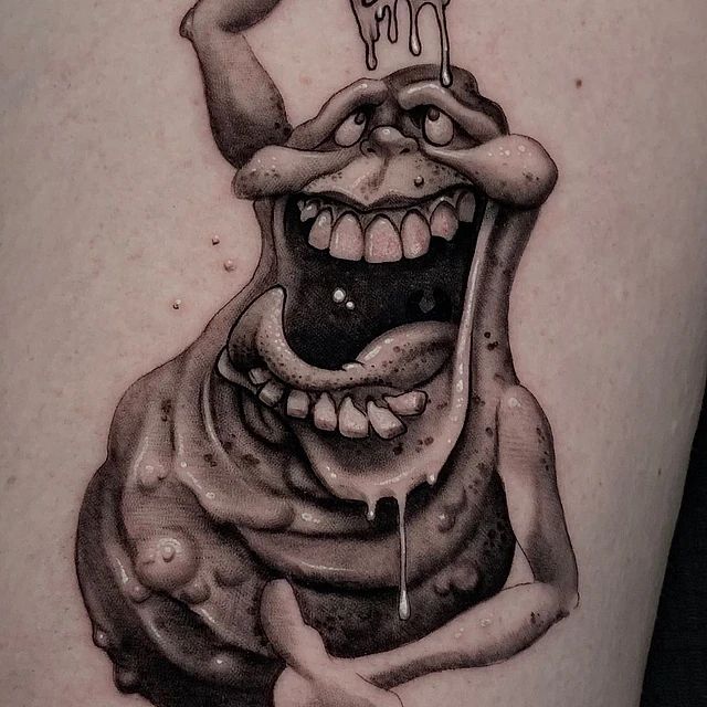 Un tatuaje en blanco y negro de un monstruo con la boca abierta.