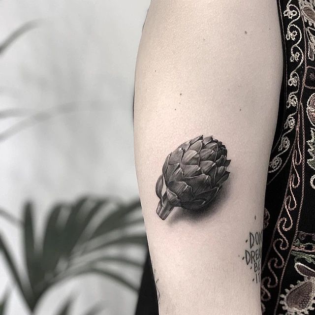 Una mujer tiene un tatuaje de una alcachofa en su brazo.