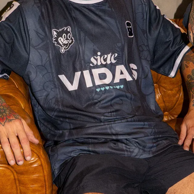 Un hombre está sentado en un sofá con una camiseta que dice siete vidas.