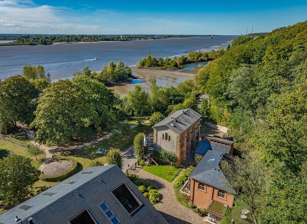Luftaufnahme von Gebäuden in der Nähe eines Flusses und üppigem Grün unter strahlend blauem Himmel.