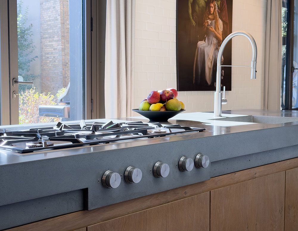 Kochfeld und Spüle aus Edelstahl in einer modernen Küche. Obstschale, Kunstwerk und Ausblick aus dem Fenster.