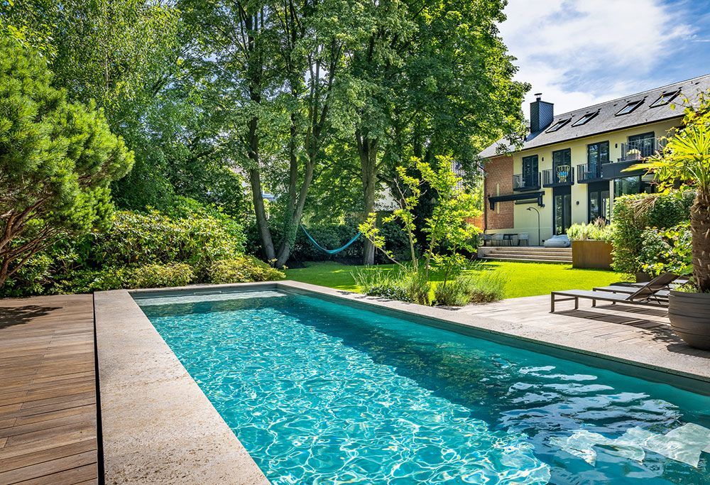 Pool in einem Garten mit Bäumen und einem Gebäude im Hintergrund.