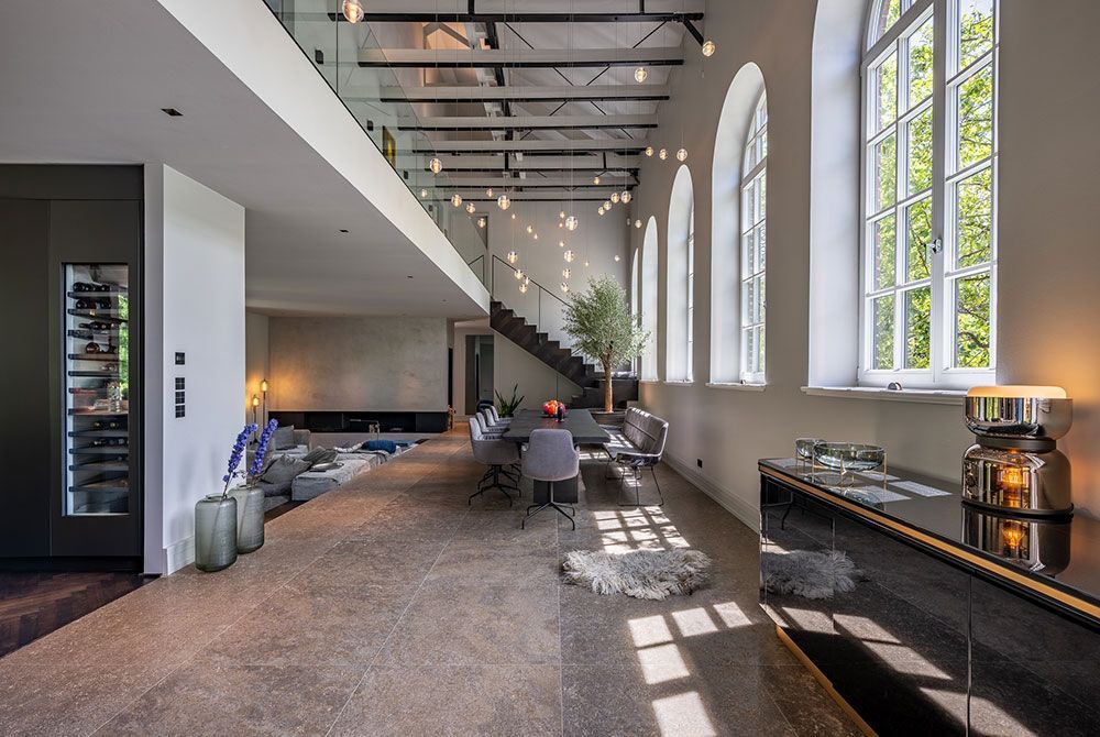 Moderner, offener Wohnbereich mit hohen Decken, großen Fenstern und einer Treppe.