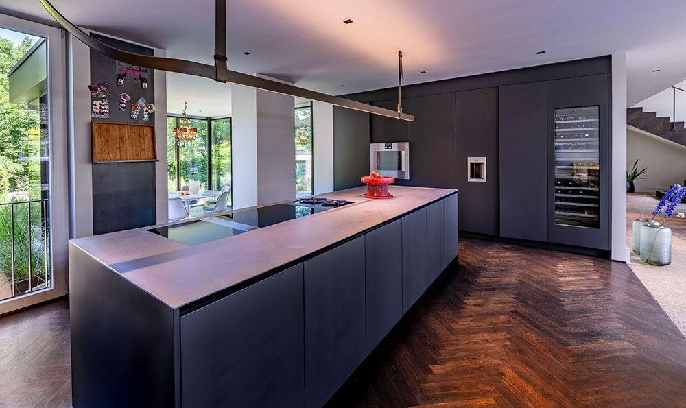 Moderne Küche mit dunklen Schränken, großer Kochinsel, Fischgrätenparkett und Weinkühlschrank.