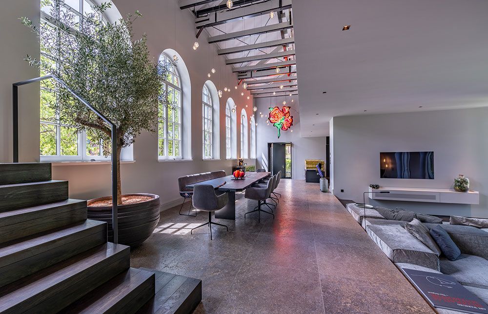 Moderner, offener Wohnbereich. Esstisch, versenkte Sitzbank, große Fenster, Olivenbaum, Kunstwerk.