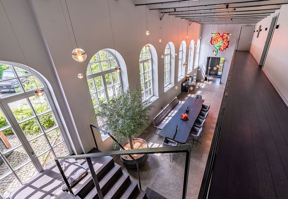 Draufsicht auf einen modernen, offenen Innenraum mit Bogenfenstern, einem langen Esstisch und einer Treppe.