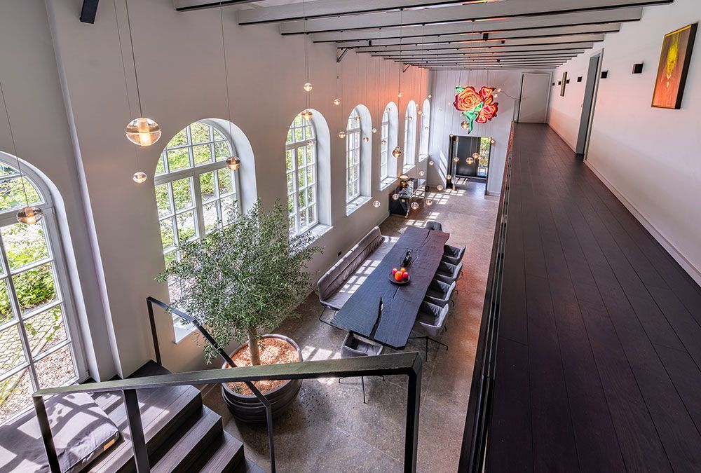 Draufsicht auf ein modernes Esszimmer mit Bogenfenstern, langem Tisch und einem Zimmerbaum.