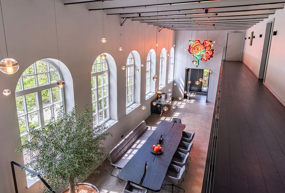 Esszimmer mit hoher Decke, langem, dunklem Tisch, Bogenfenstern und einem großen Rosenbild.