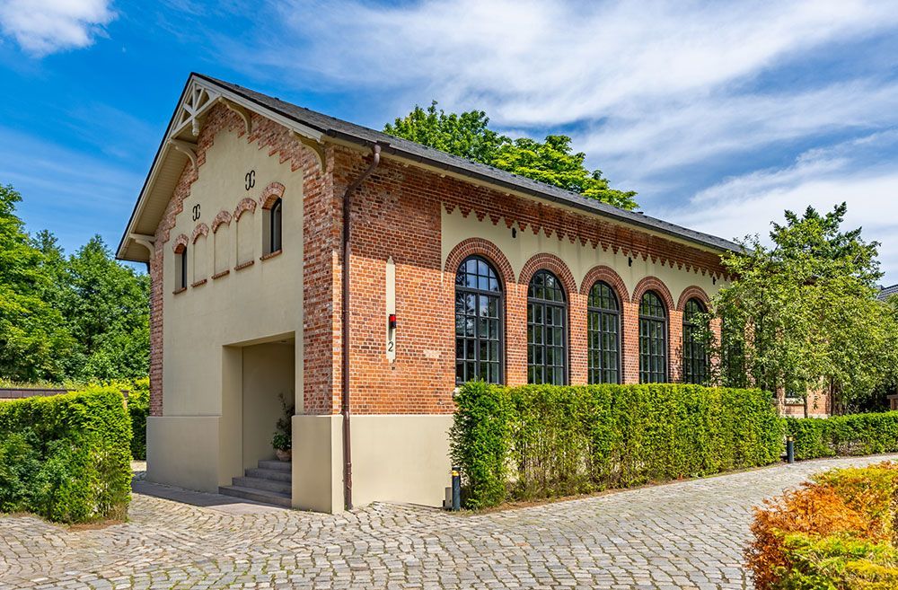 Ein Gebäude aus Backstein und Stuck mit Bogenfenstern, akkurat geschnittenen Hecken und blauem Himmel.