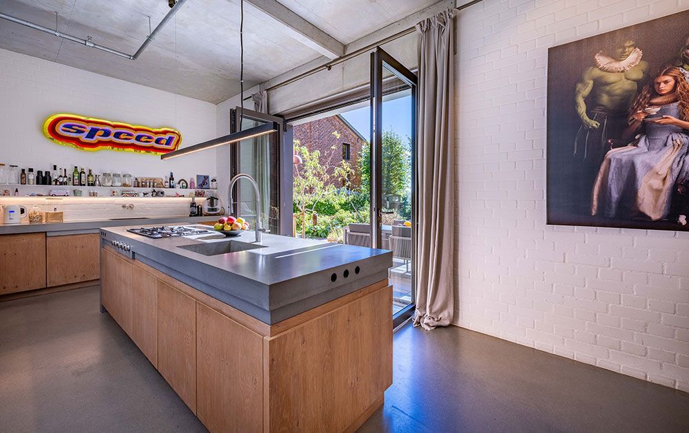 Moderne Küche mit Kochinsel und Zugang ins Freie. Holzschränke, Betonarbeitsplatte, farbenfrohes Geschwindigkeitsschild.