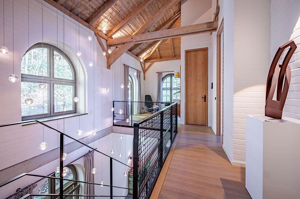 Innenflur mit Bogenfenstern, Holzbalken und Metallgeländer. Dekorative Kugellampen hängen daran.