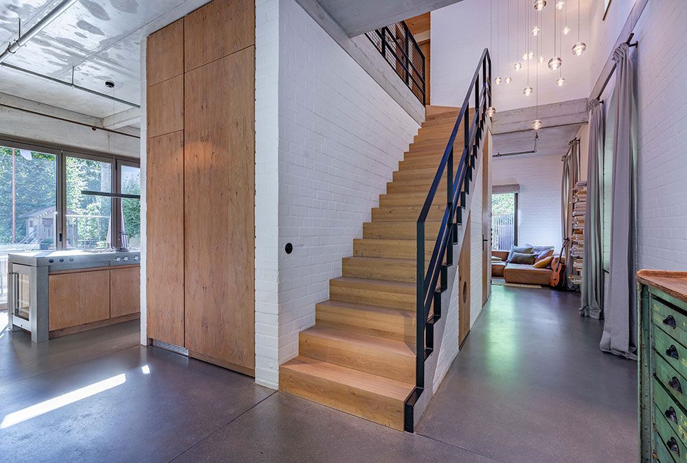 Modernes Interieur mit Holztreppe, Holzvertäfelung, Sichtmauerwerk und Betonboden.