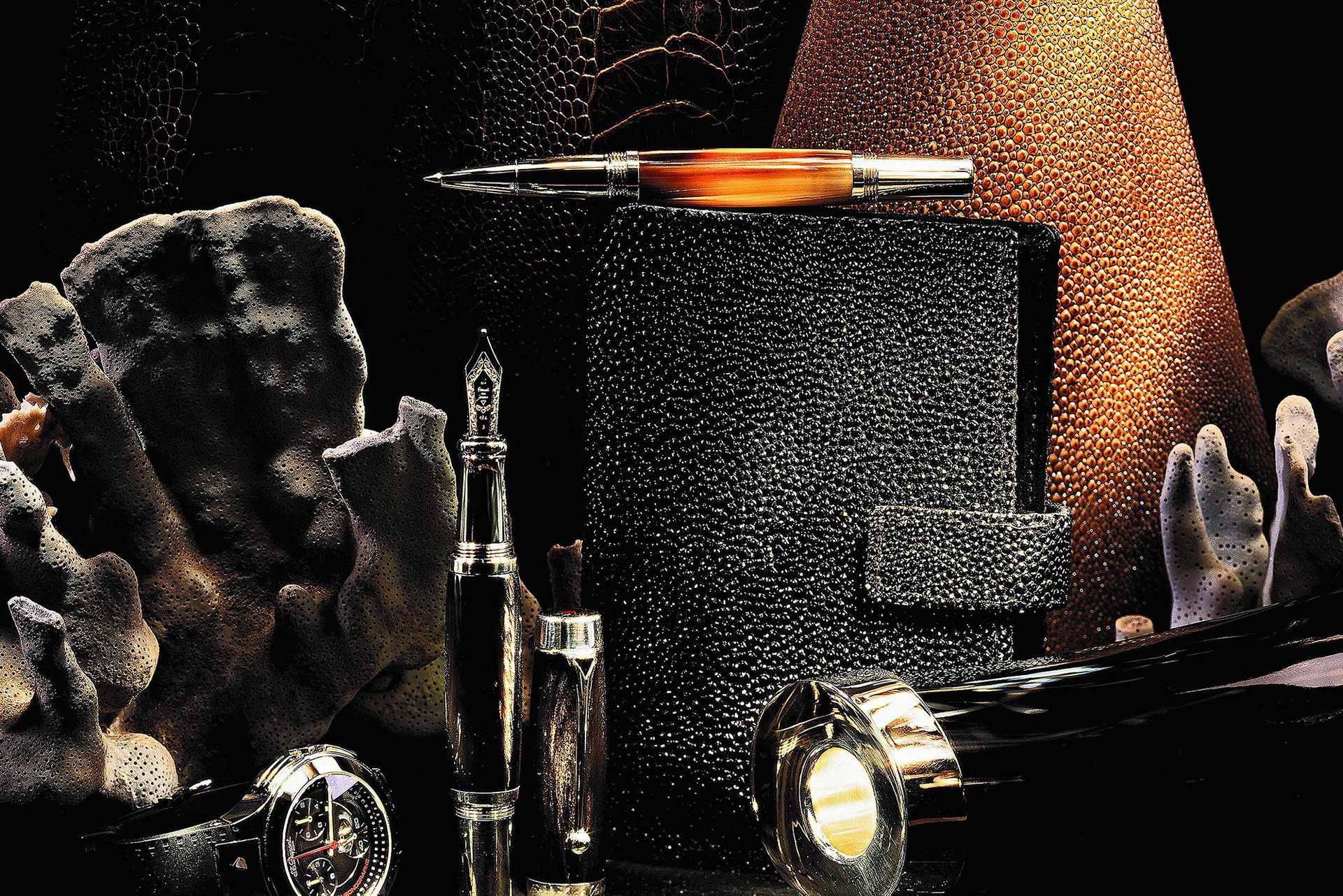 Dunkler Schreibtisch mit Notizbuch, Füllfederhalter und anderem Schreibzubehör.