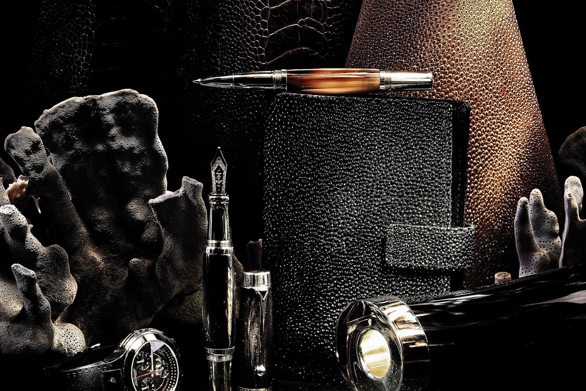 Stillleben mit Gegenständen, darunter ein Stift und eine Uhr, vor einem strukturierten dunklen Hintergrund.