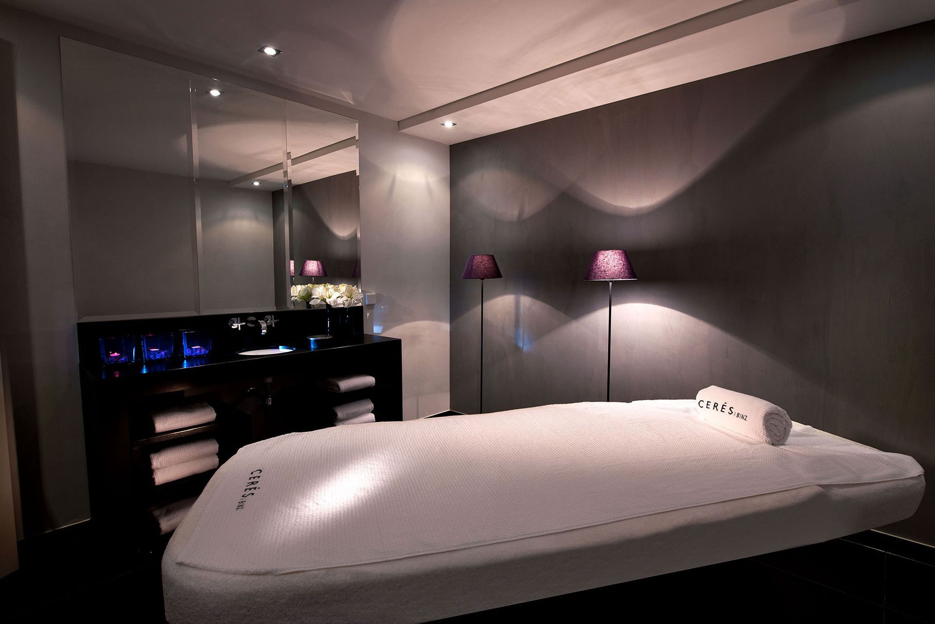 Wellnessraum mit Massageliege, Handtüchern und dekorativen Lampen.