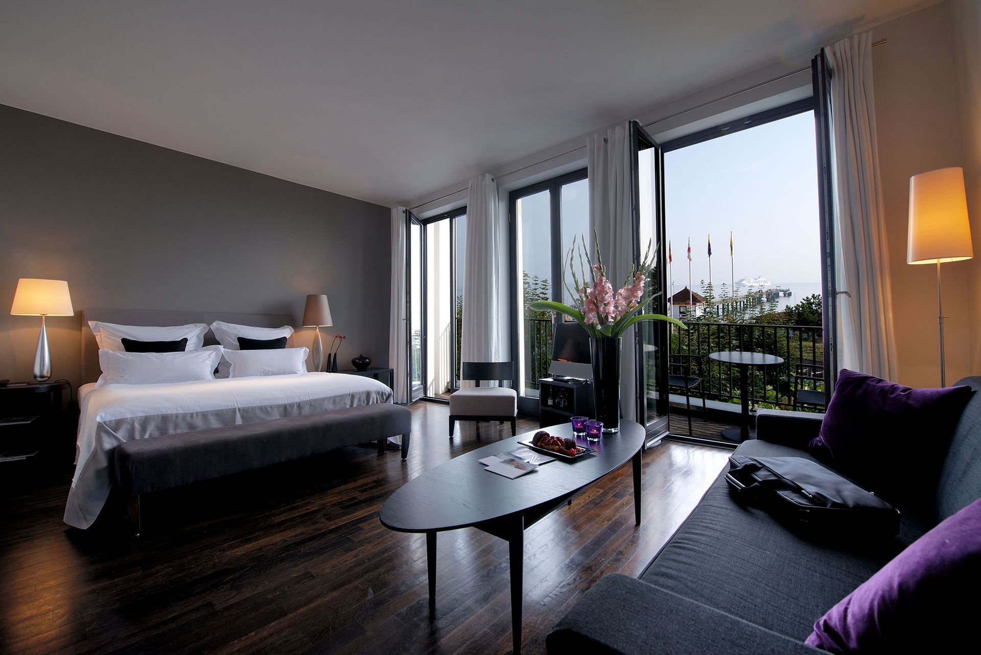 Hotelzimmer mit Bett, Sofa, Tisch und Balkon mit Blick ins Freie.