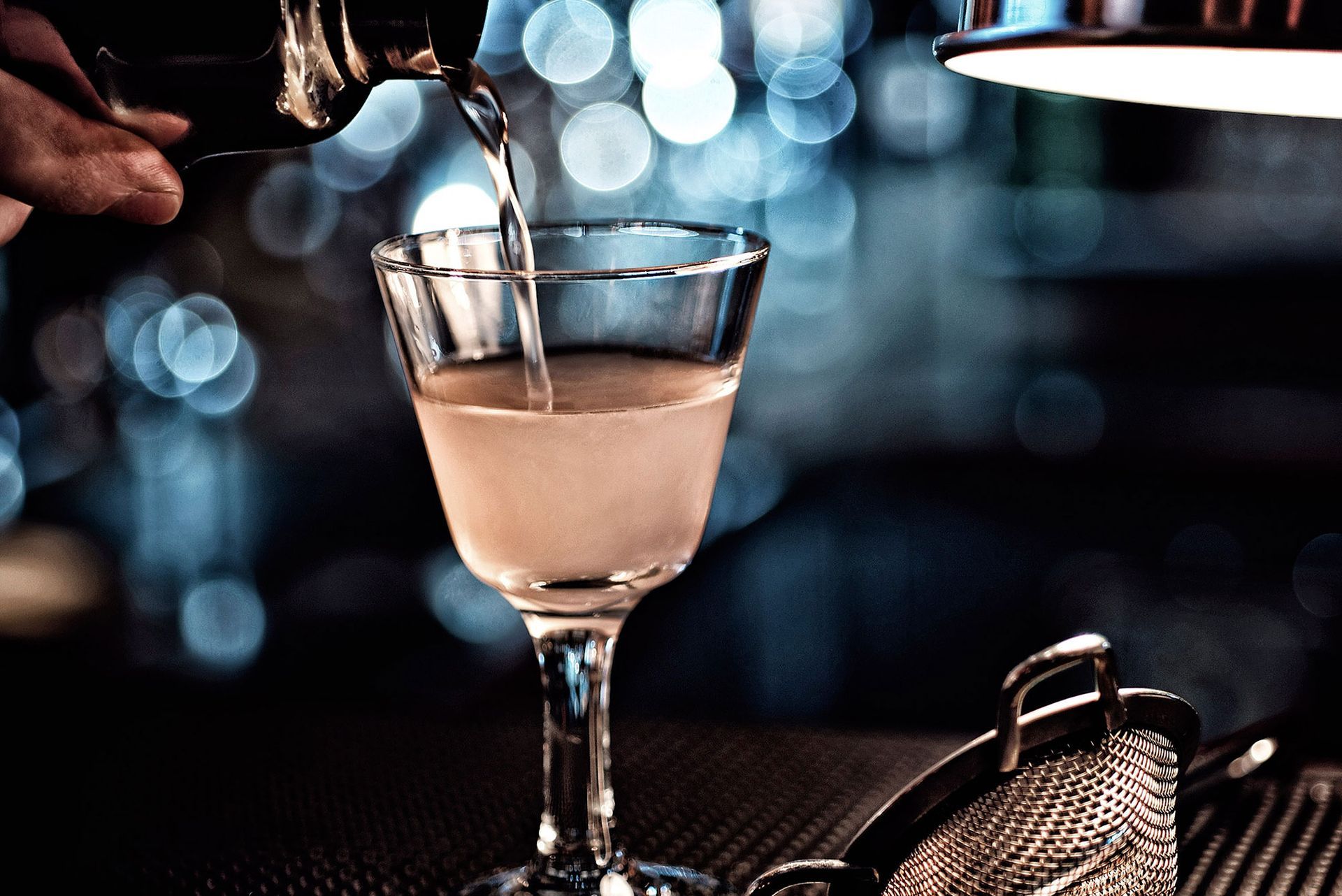 Ein Barkeeper schenkt einen Cocktail in ein Stielglas ein, Barszene, Bokeh-Hintergrund.