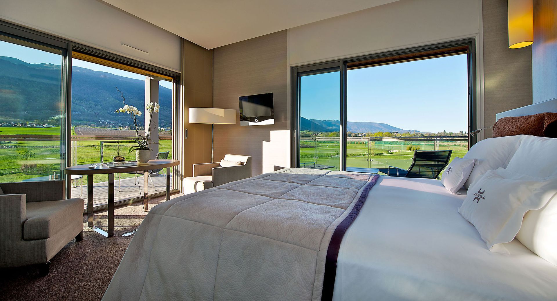 Hotelzimmer mit Bett und großen Fenstern mit Blick auf die grüne Landschaft.