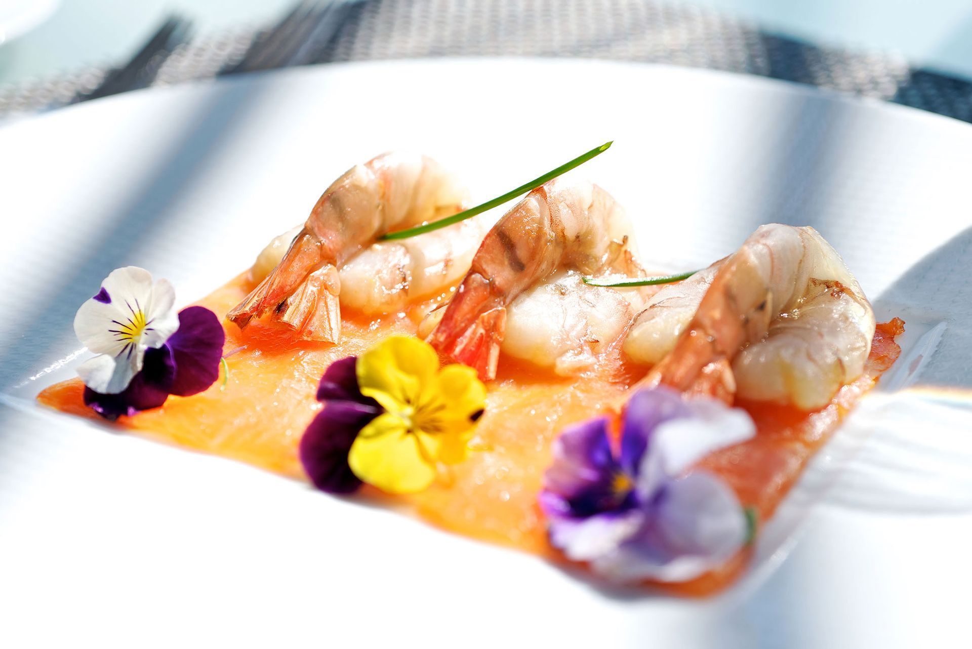 Vorspeise aus Garnelen und Lachs, garniert mit essbaren Blüten, auf einem weißen Teller.