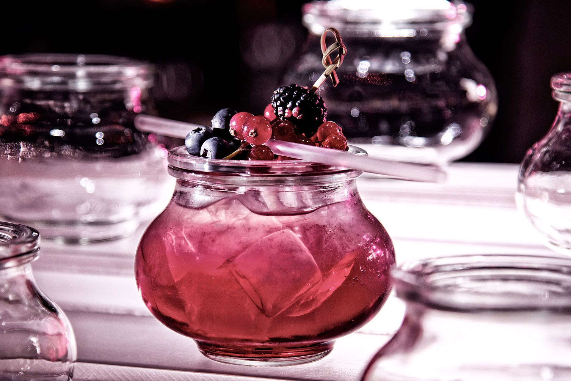Cocktail in einem Glasgefäß mit Beeren und einem Rührstab, auf einer Bar platziert.