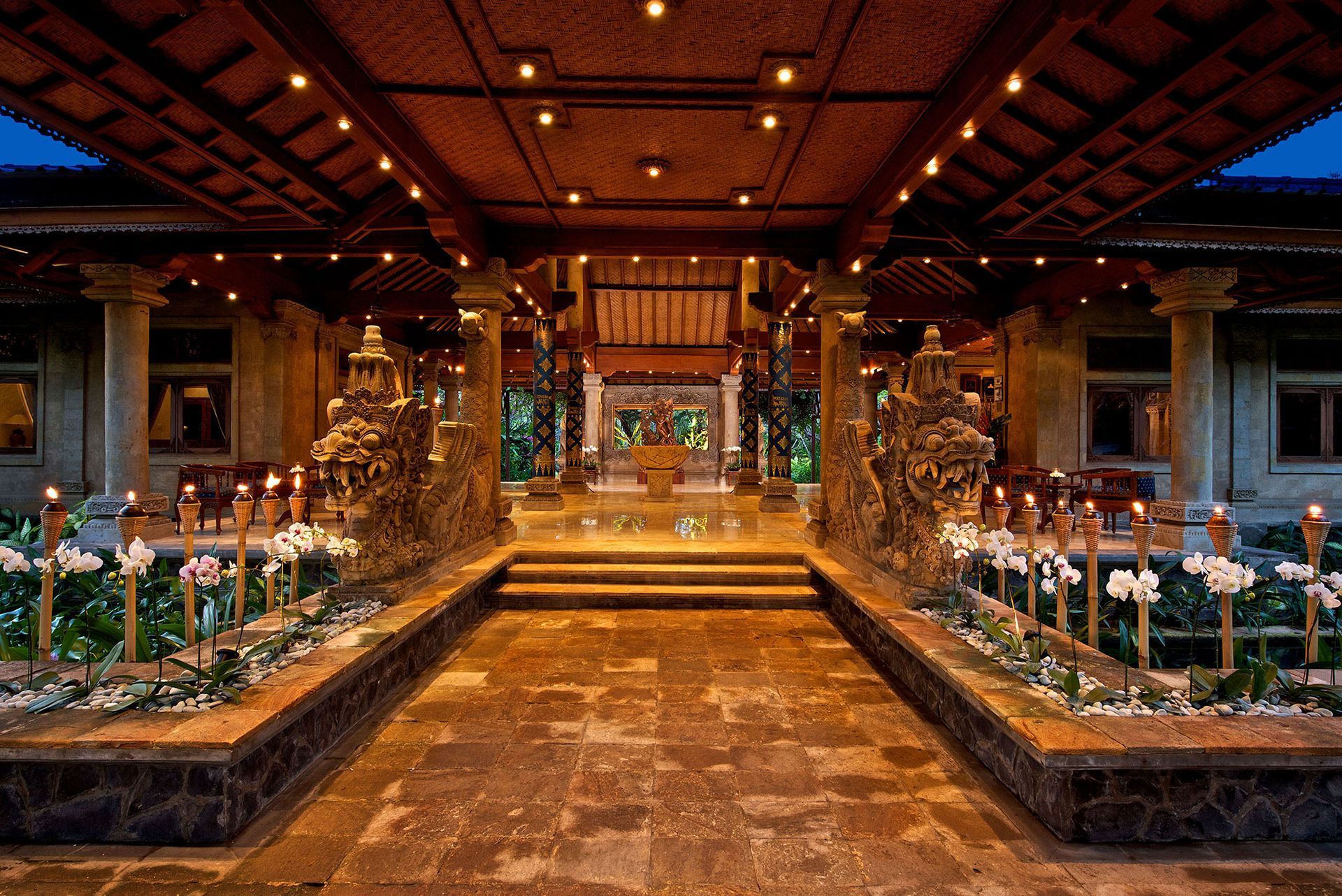 Steineingang zu einem Resort, beleuchtet mit warmem Licht und Blumenschmuck.