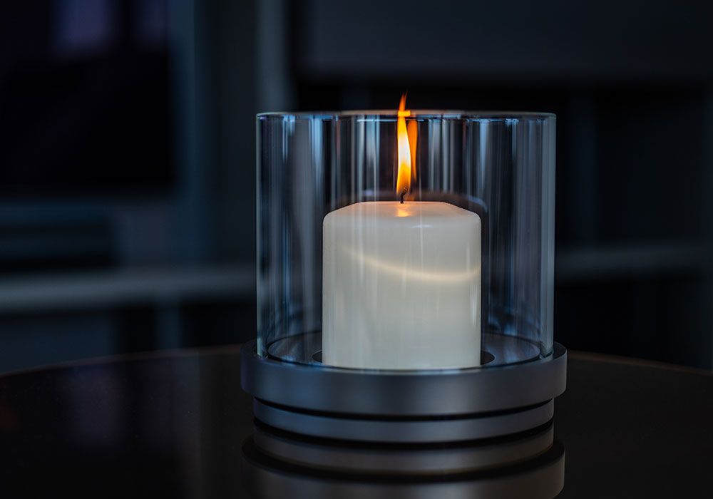 Eine brennende weiße Kerze in einem durchsichtigen Glaszylinder stand auf einem dunklen Tisch.