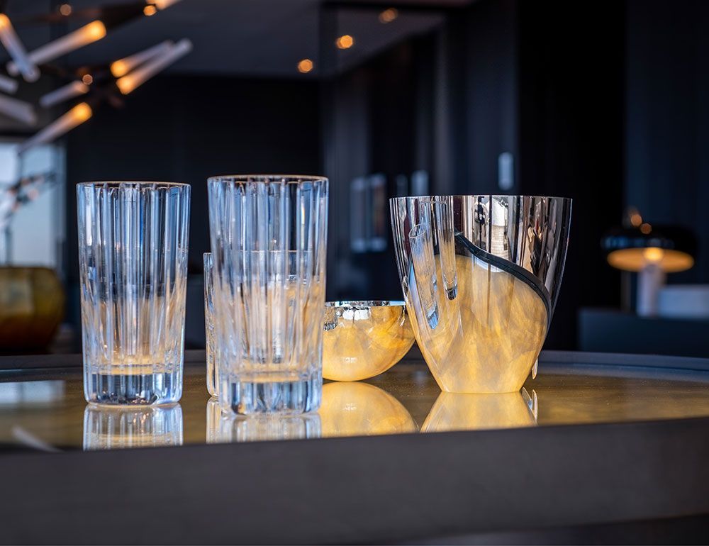 Kristallgläser auf einer spiegelnden Oberfläche vor verschwommenem Hintergrund. Zwei hohe Gläser und eine Vase.