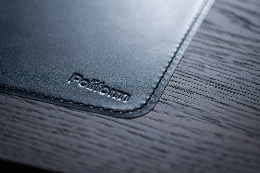 Nahaufnahme eines schwarzen Schreibtischunterlage aus Leder mit dem geprägten Wort „Poliform“ in der Ecke auf einer Holzoberfläche.
