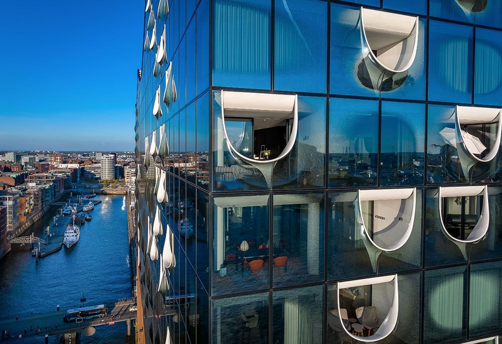 Modernes Glasgebäude mit einzigartiger Fenstergestaltung und Blick auf einen Wasserweg und die Stadt.