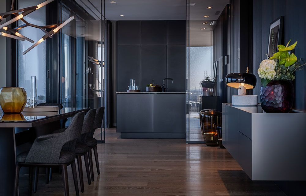 Modernes, dunkel getöntes Interieur mit Küche, Essbereich und Flur; Holzboden, Glaswände und stilvolle Einrichtung.