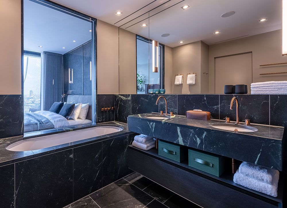 Luxuriöses Badezimmer mit schwarzem Marmor, Doppelwaschbecken, Badewanne und freiem Blick zum Schlafzimmer.