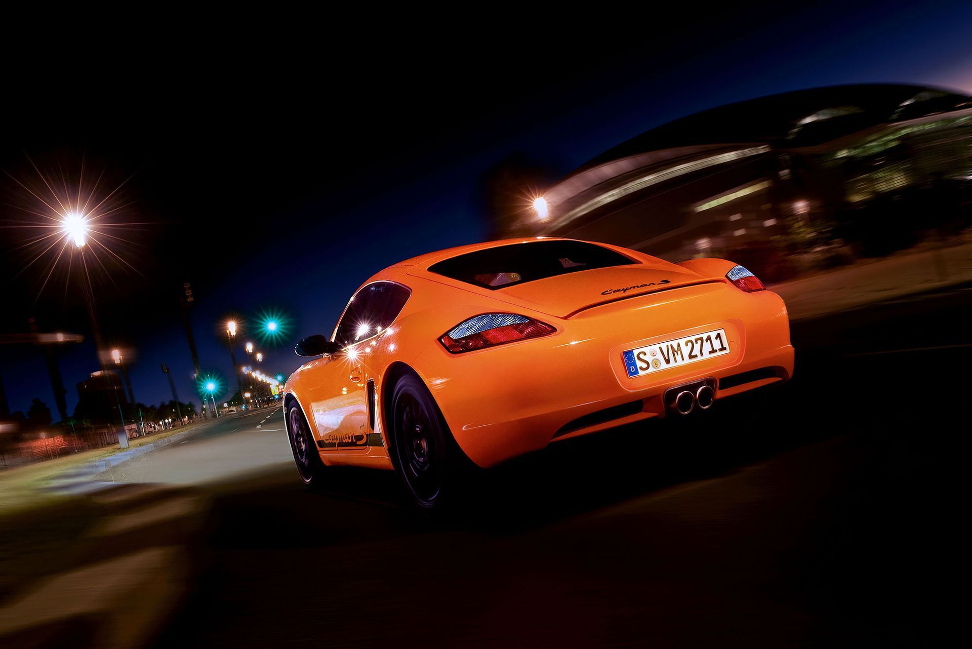 Ein orangefarbener Porsche-Sportwagen fährt nachts auf einer dunklen Straße.