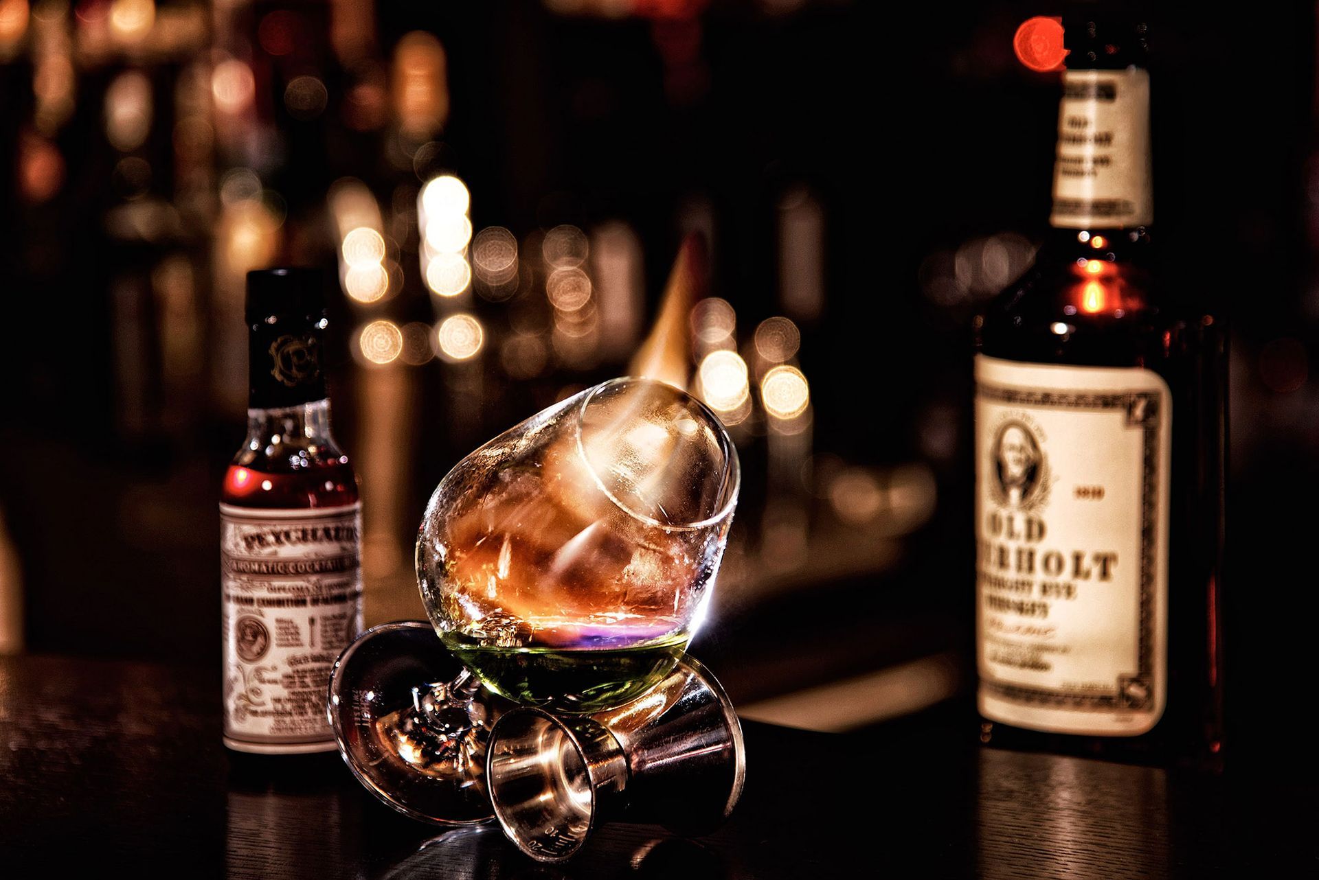 Whiskey-Cocktail mit brennender Flamme, Bitter und einer Flasche Whiskey auf einer dunklen Bar.