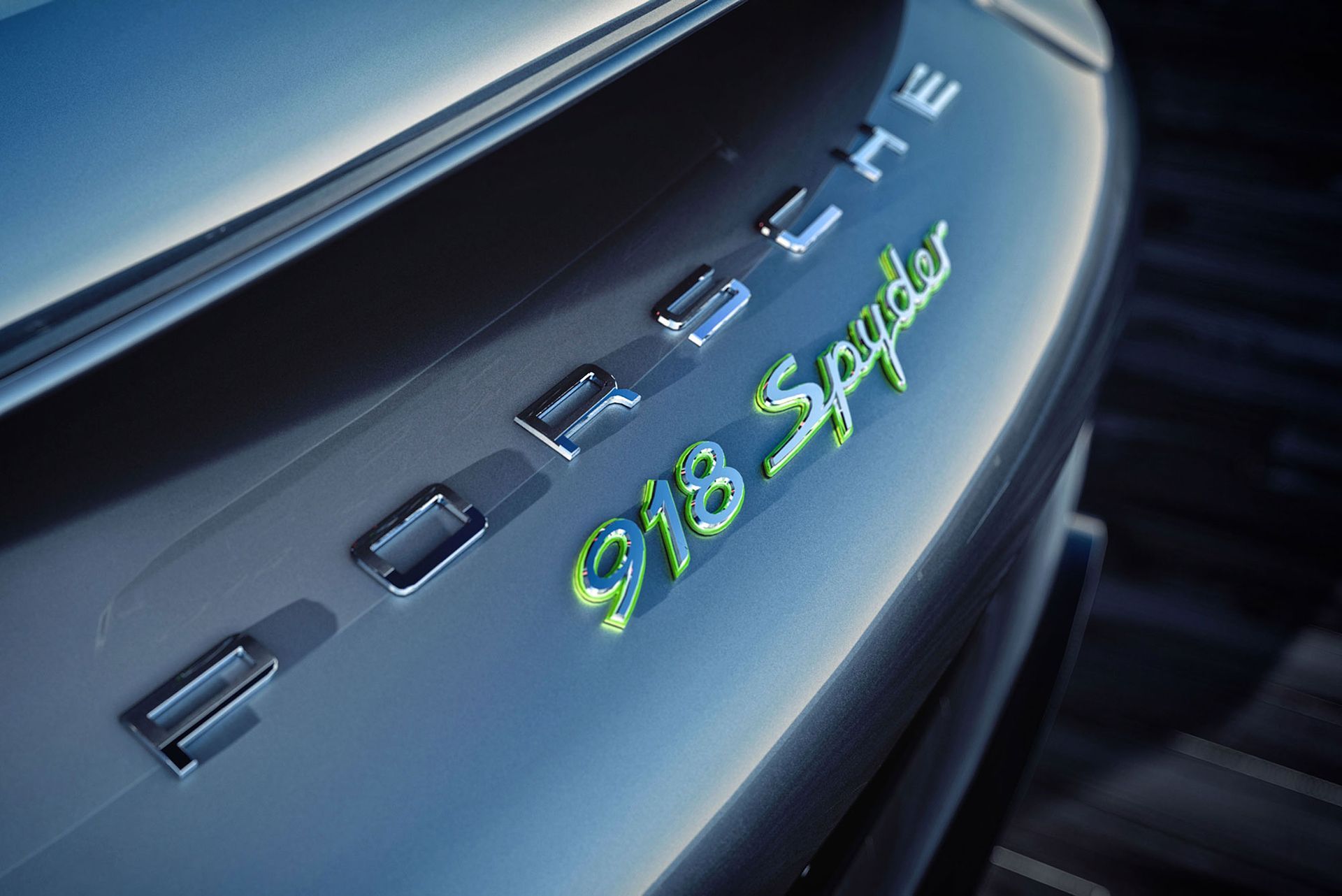 Nahaufnahme des Hecks eines silbernen Porsche 918 Spyder mit den Logos „PORSCHE“ und „918 Spyder“. Grüne Akzente.