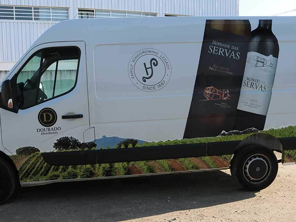 Uma van branca com uma garrafa de vinho na lateral está estacionada na beira da estrada.